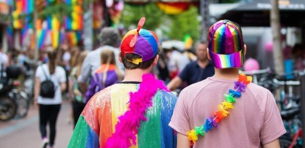 Twee mensen, gezien op de rug, versiert met regenboog petjes, shirt en slingers op straat