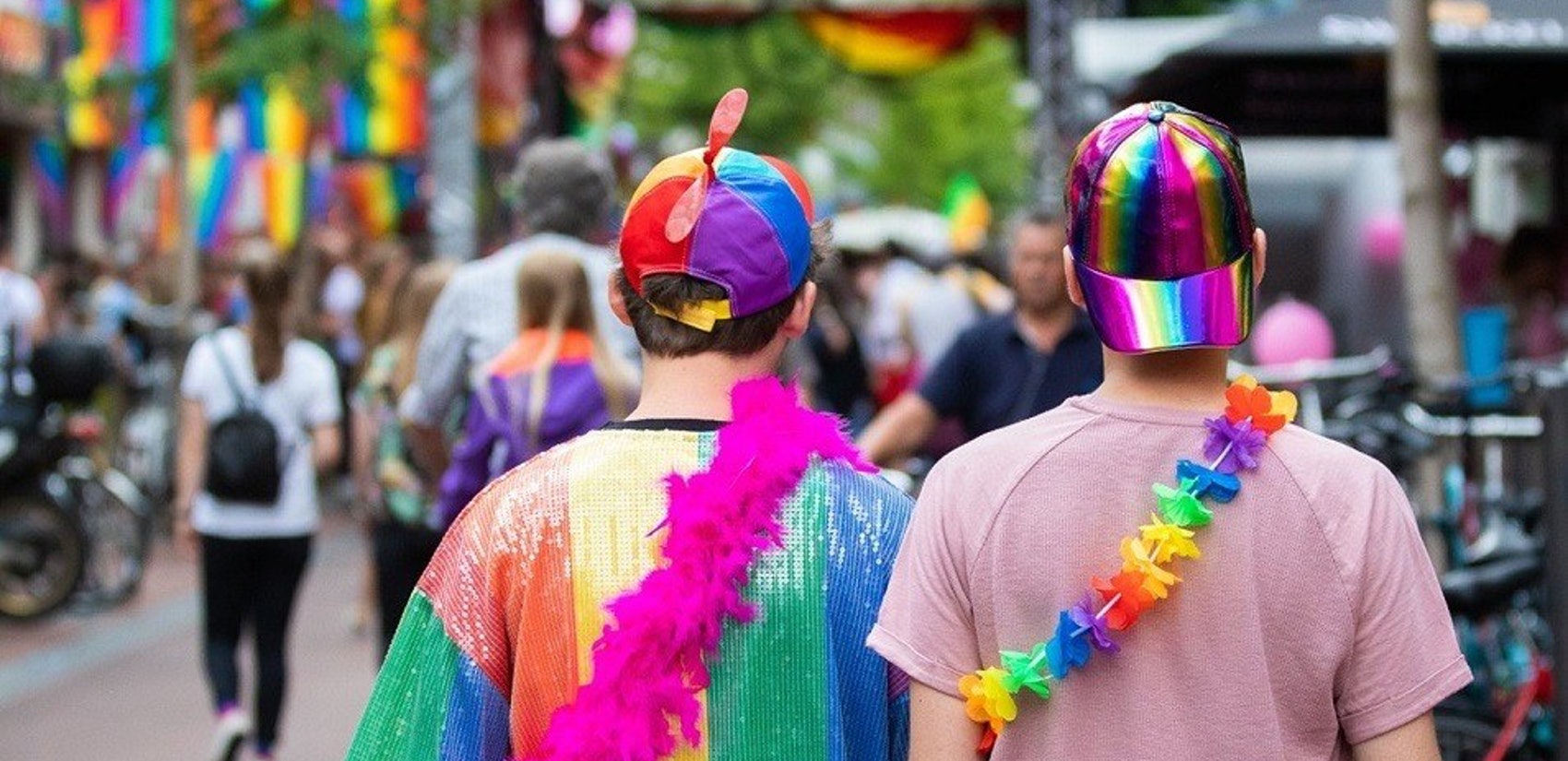 Twee mensen, gezien op de rug, versiert met regenboog petjes, shirt en slingers op straat